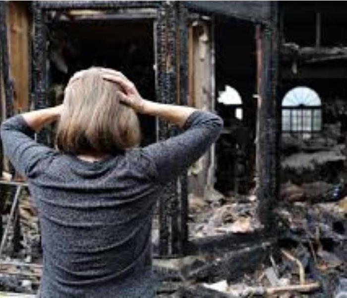 woman holding her head with both hands and observing the damage as a result of a fire to her home 